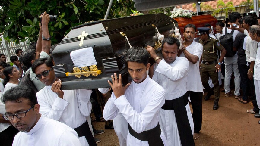 Men in white robes carry a black coffin on their shoulders.