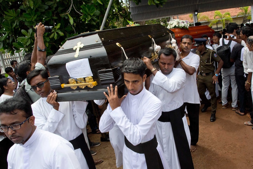 Men in white robes carry a black coffin on their shoulders.