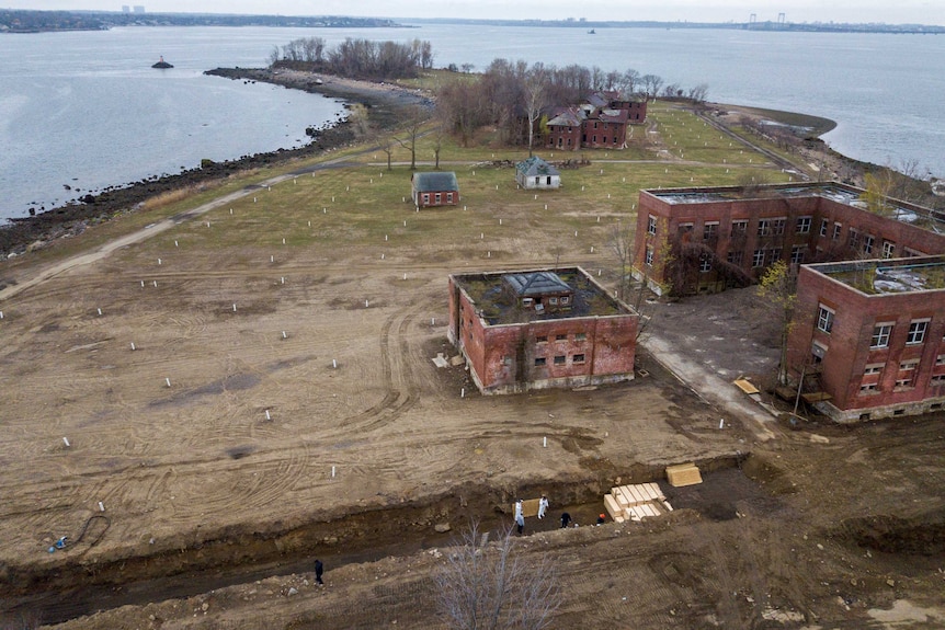 A drone shot of a small island with people burying caskets in a mass grave