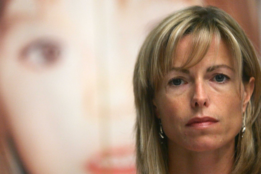 Kate McCann looking serious in front of a poster of her daughter's face