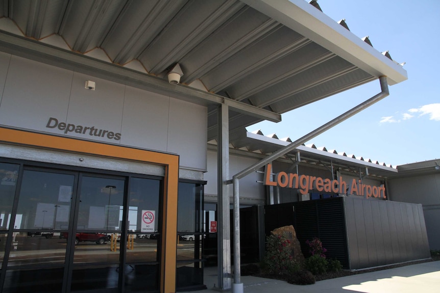 The outside of a small regional airport building with signs that say "Longreach Airport" and "Departures" above automatic doors.
