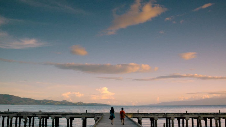 Two figures stand on a large pier in Indonesia at sunset in a still image from the film Salawaku.
