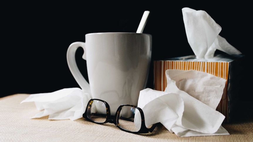 A teacup, glasses and box of tissues with crumpled tissues around the edges.