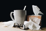 A teacup, glasses and box of tissues with crumpled tissues around the edges.