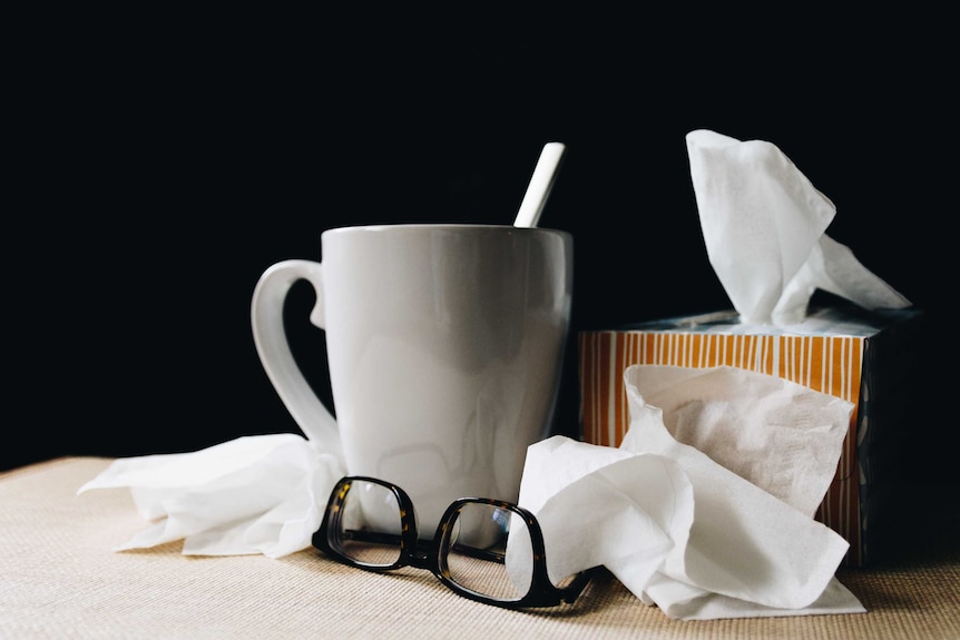 A teacup, glasses and box of tissues with crumpled tissues around the edges.