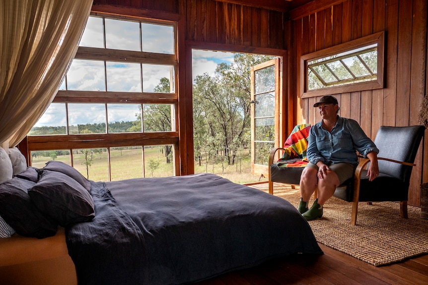 A woman sits in a timber cabin bedroom.