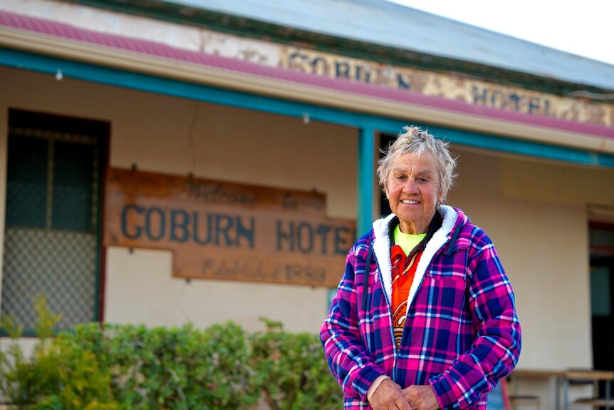 A white woman wearing a purple jacket standing in front of the Coburn Hotel.