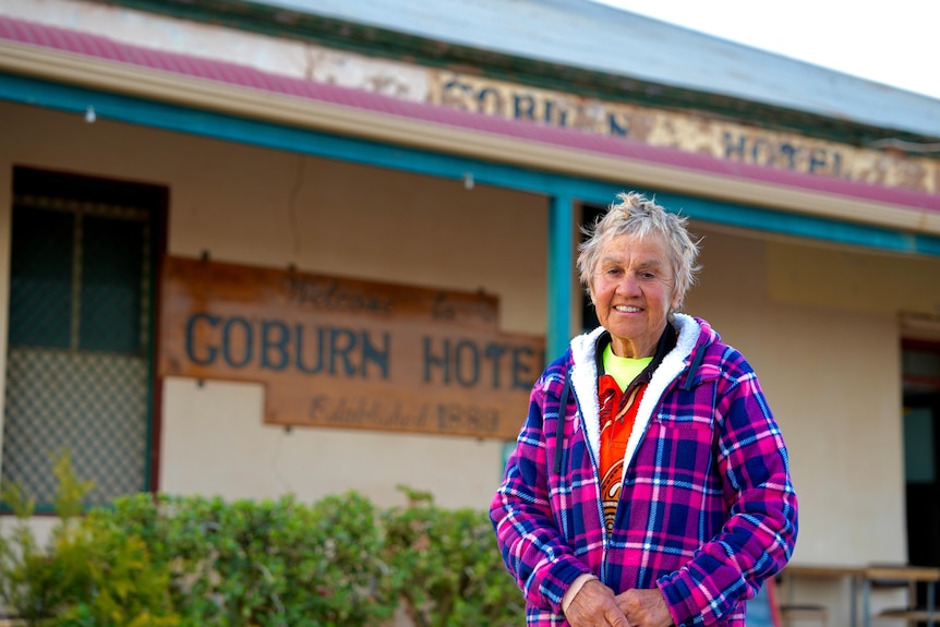 A white woman wearing a purple jacket standing in front of the coburn hotel.