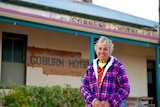 A white woman wearing a purple jacket standing in front of the Coburn Hotel.