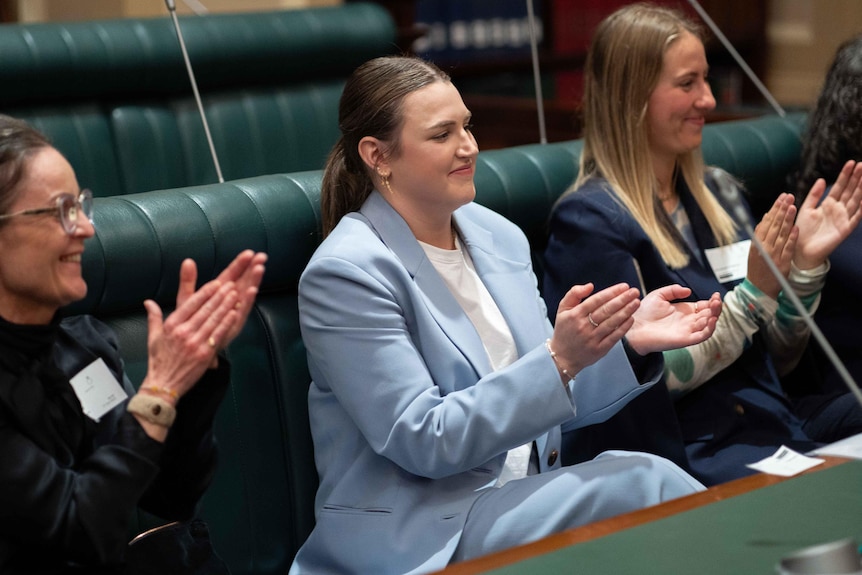 Three women smiling and clapping sitting on a bench inside South Australia's parliament house. 