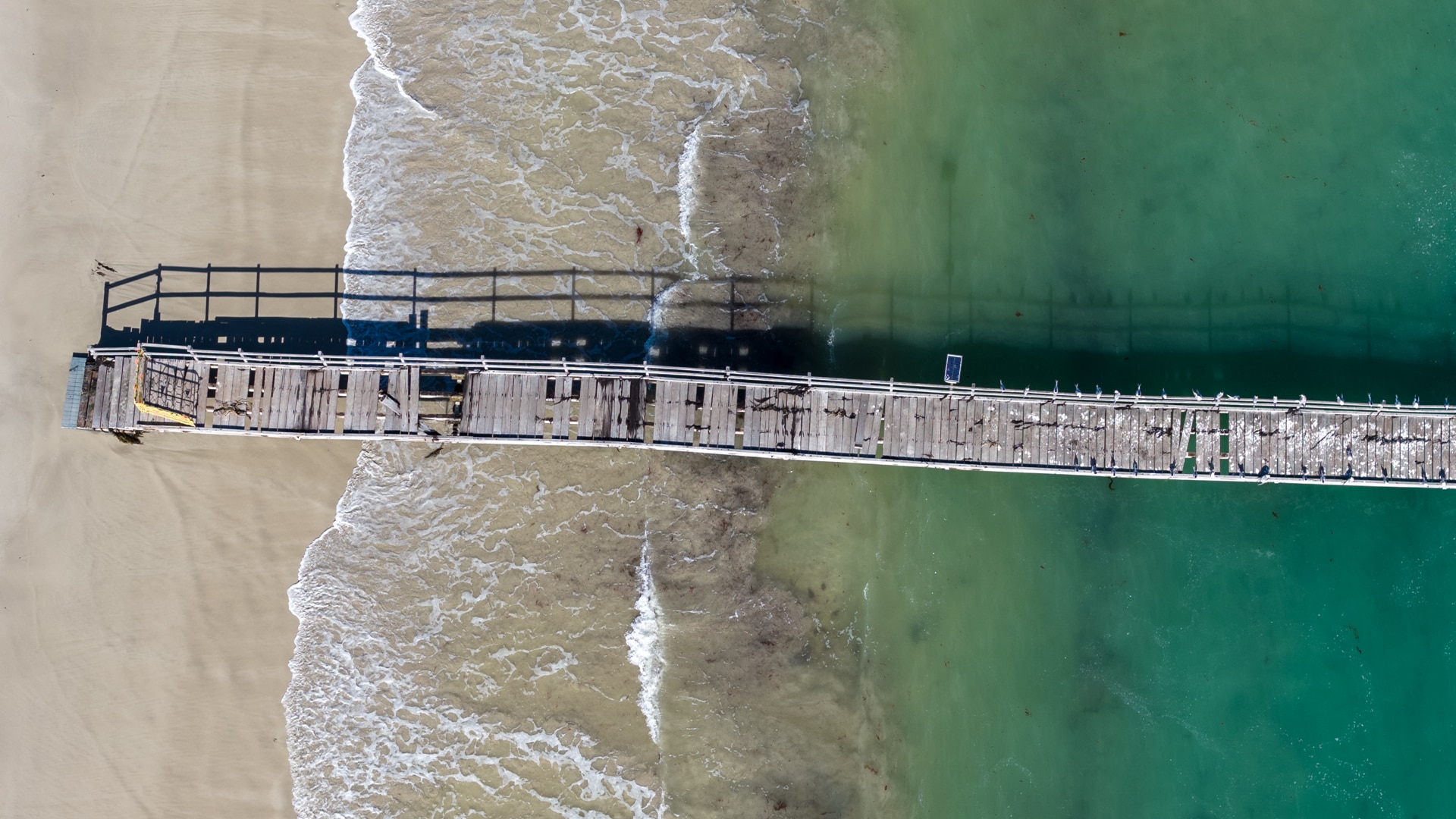 A drone shot of a jetty with planks missing. 