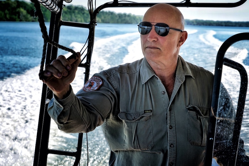 Stewart Woerle wears a dark green shirt and aviator sunglasses, on a boat, with the wake and ocean pictured behind him.