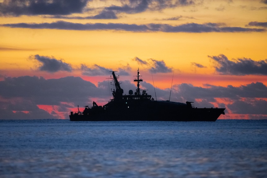 A navy ship at sea silhouetted by a sunset.