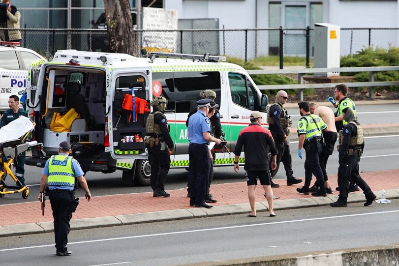 Police officers walk a shirtless man to an ambulance.