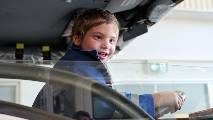 a boy sits behind the wheel of a fire truck