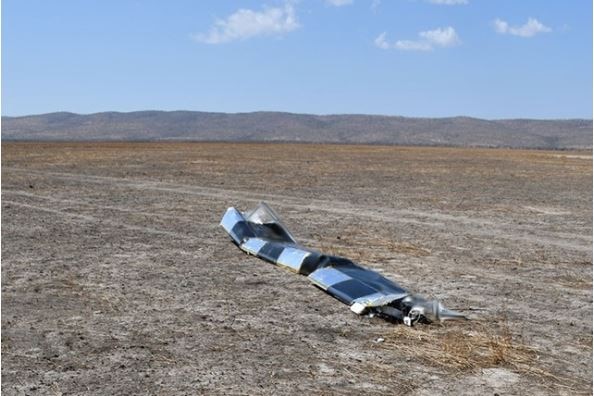 Image of a broken wing of a crashed aircraft sitting in isolated bushland, with hills in the background.
