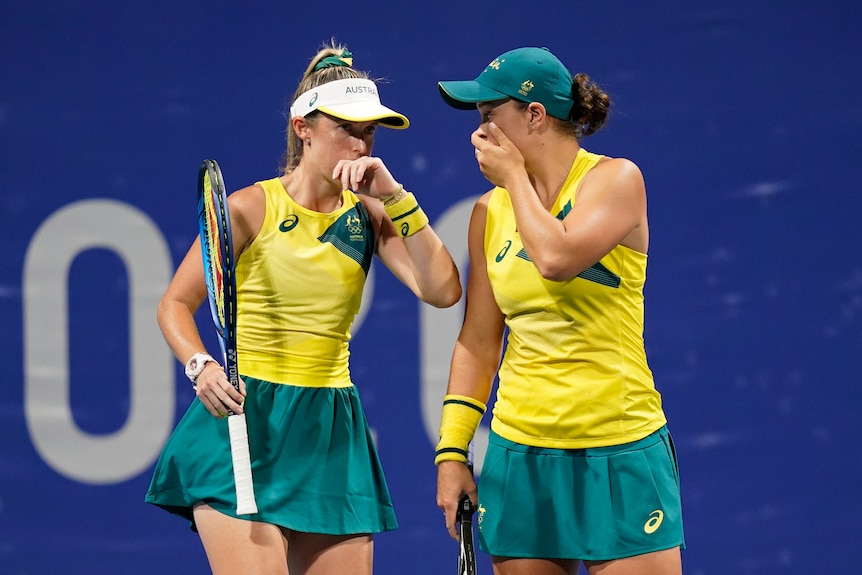 Storm Sanders and Ash Barty cover their mouths as they speak to each other on the court during doubles at the Tokyo Olympics.