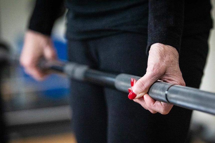 A woman's hands with long red fingernails grips a weight bar