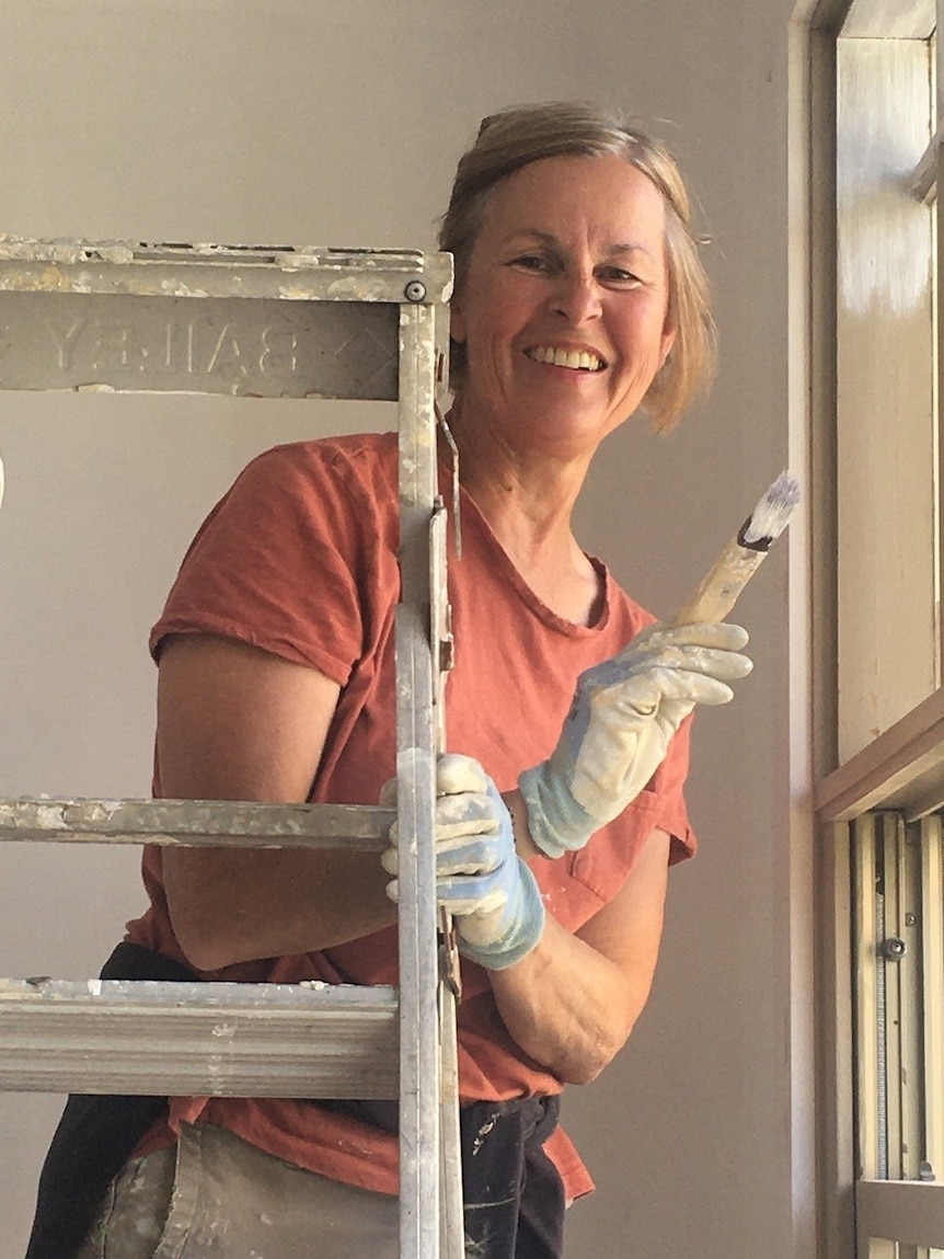 Anne Callahan smiles at the camera with a paint brush in hand