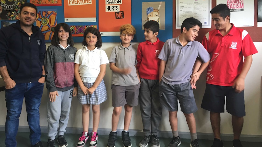 Six Yazidi refugee students in classroom smiling with English language teacher