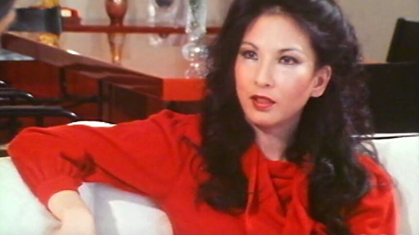 A screenshot from a grainy VHS video shows Rose Hancock Porteous in a bright red silk shirt.