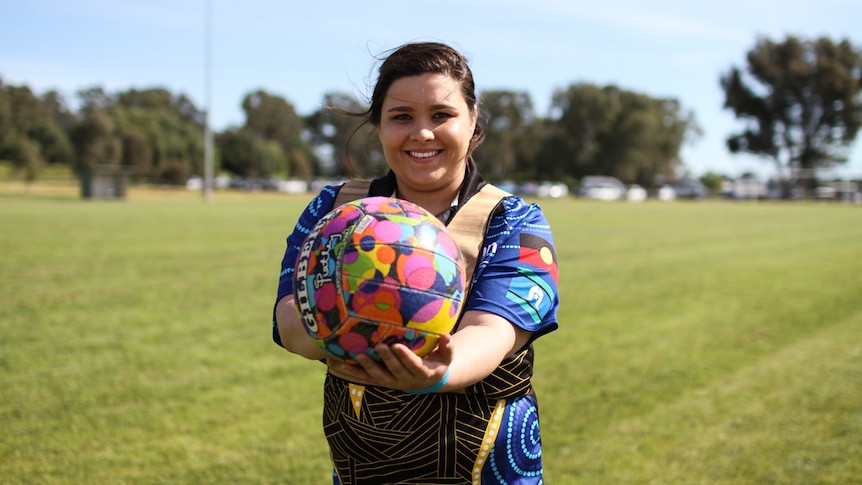 Lowana Clarke, 26 from Team Beyond Blue stands holding a netball outfront.