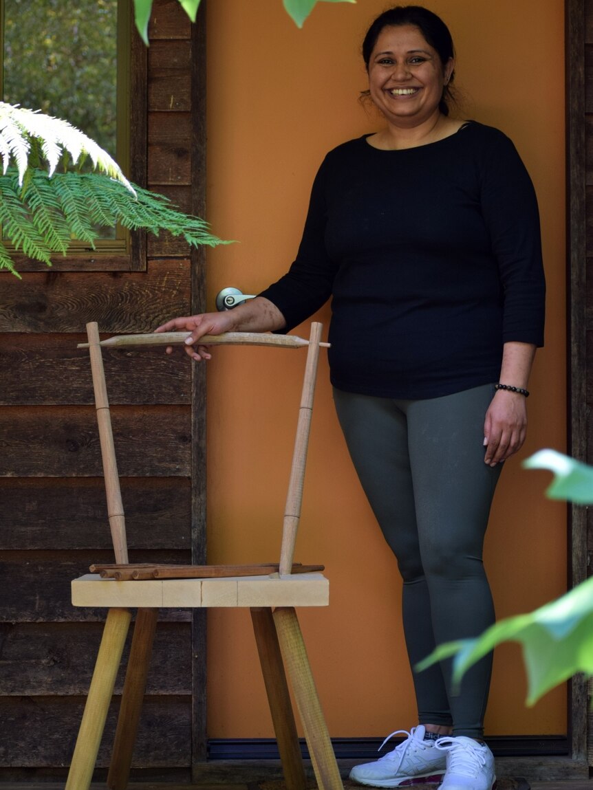 Woman standing smiling next to handmade chair under construction