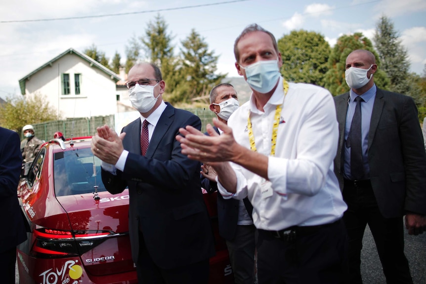 French Prime Minister Jean Castex (left) and race director Christian Prudhomme applaud Tour de France riders.