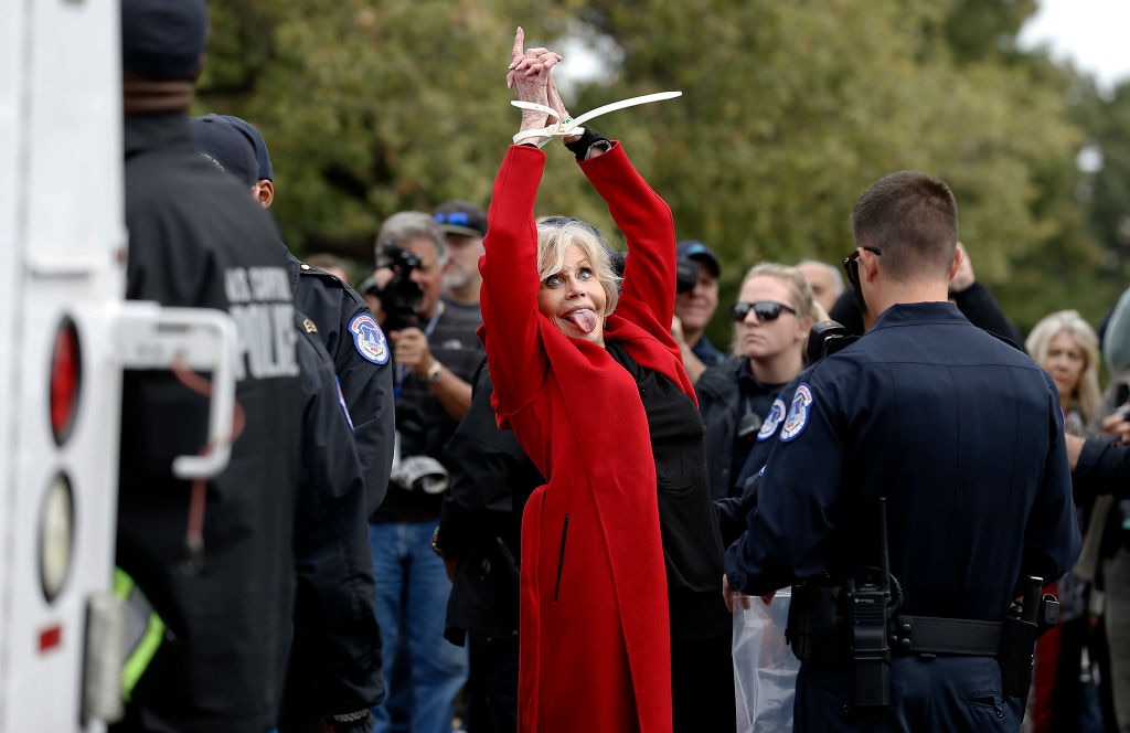 Hollywood celebrity Jane Fonda in handcuffs protesting while wearing a red jacket.