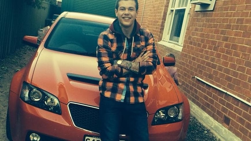 A young man sitting on the bonnet of an orange car