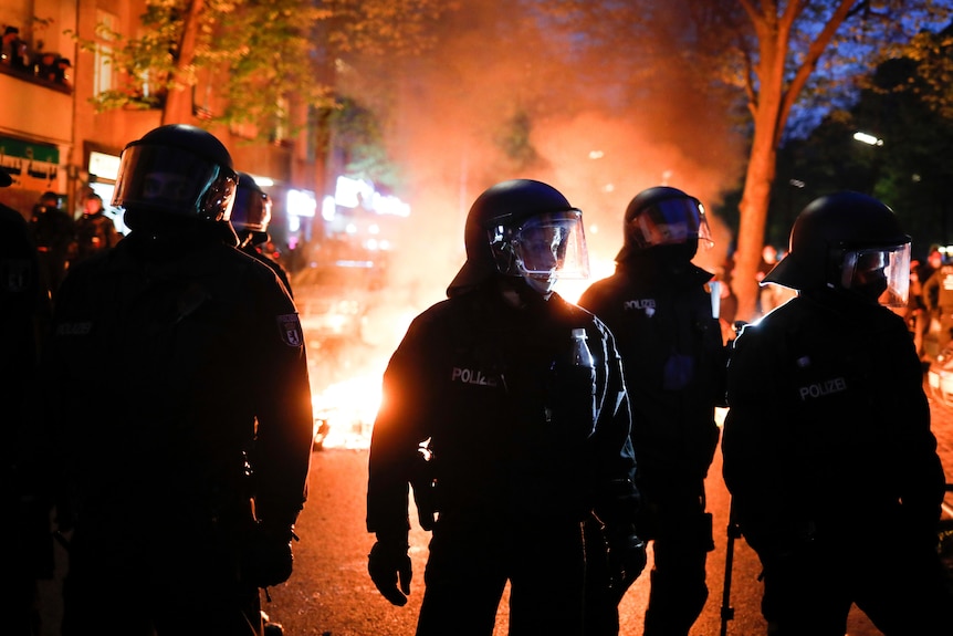 Police officers stand in front of a fire set up by demonstrators.