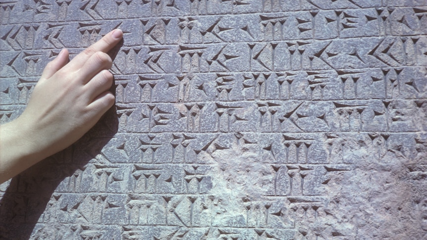 A finger points at some cuneiform inscriptions.