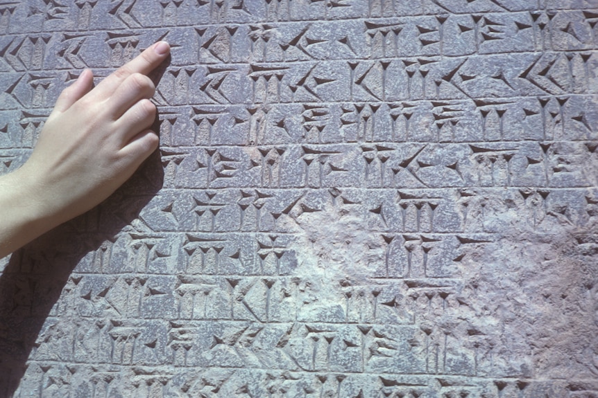 A finger points at some cuneiform inscriptions.