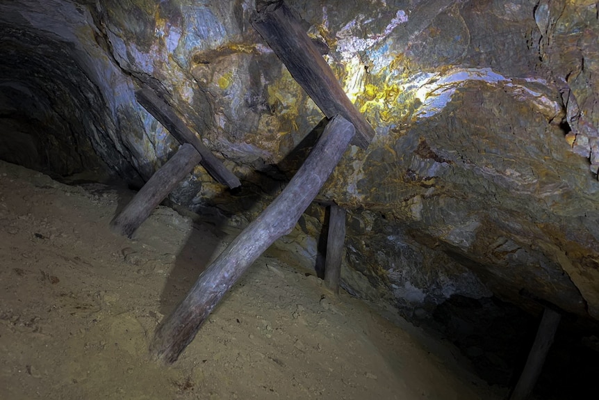 wooden poles prop up against the ceiling of an underground mine.