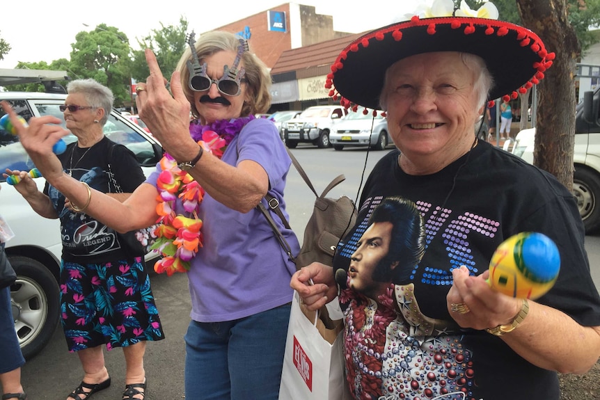 Three women dressed in Elvis T shirts dancing on the footpath in Parkes