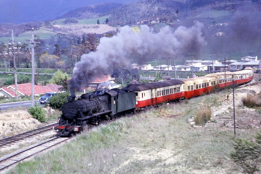 A steam strain belching grey smoke. It has a black engine and red and cream carriages behind it.