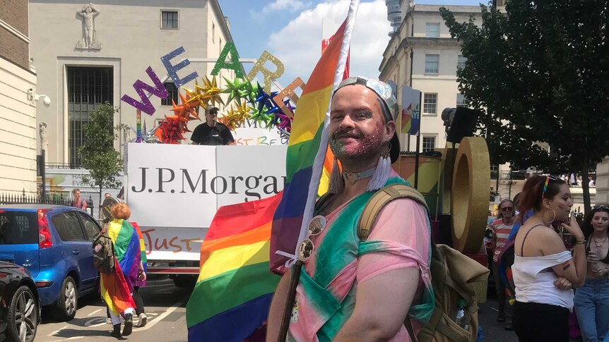 A young gender non-binary person in a colourful outfit poses on a London street in the foreground of pride parade.