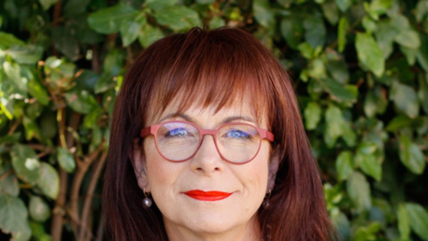 A middle-aged woman with brown hair and spectacles looks at the camera.