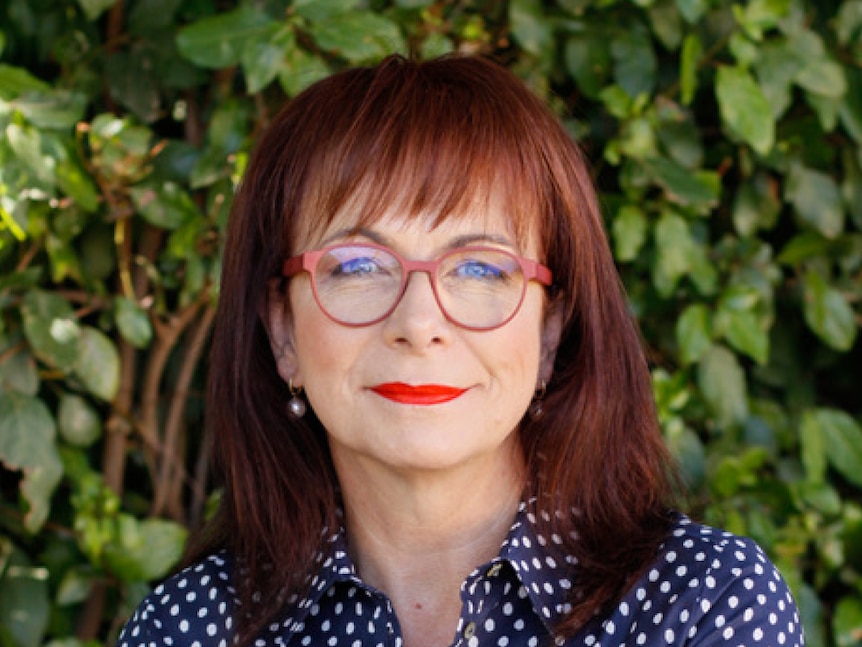 A middle-aged woman with brown hair and spectacles looks at the camera.