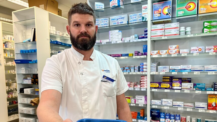 A pharmacist standing behind a counter holding a prescription basket towards the camera