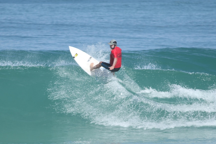 A man surfing on a wave in a red rash-shirt