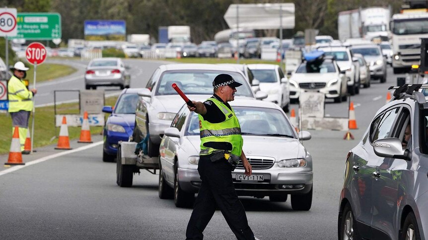 A Queensland police officer directs traffic as motorists queue at a border checkpoint at Coolangatta on the Gold Coast.
