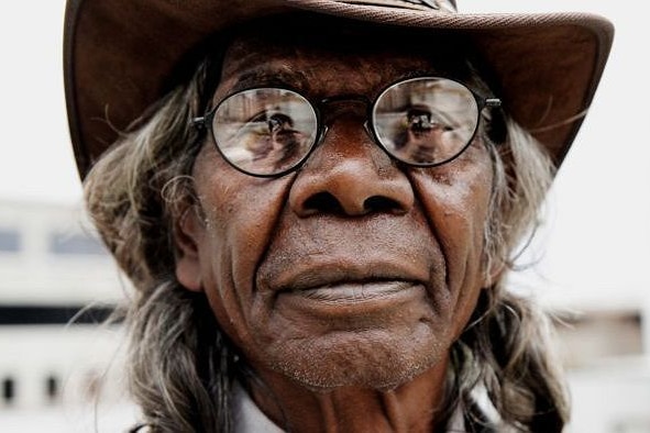 A facial close up of a bespectacled David Gulpilil and part of his Akubra hat