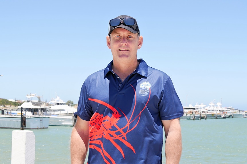 A man stands in front of some boats on a jetty.