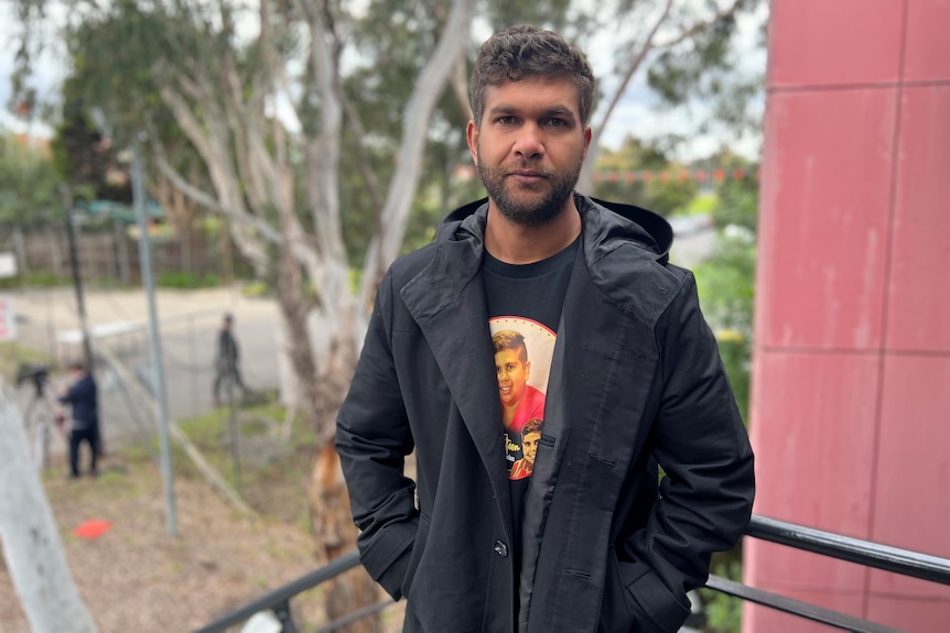 A man standing and wearing a shirt with a boy's face printed on it.