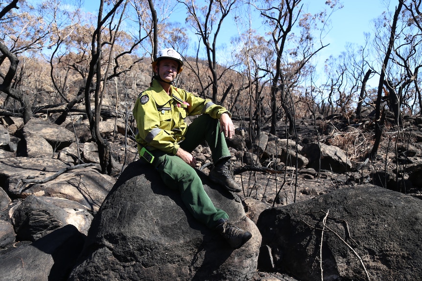 A man in a firefighting uniform sits on top of a rock.
