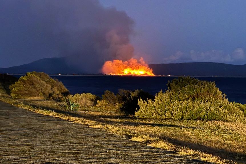 A bushfire burns across a body of water.