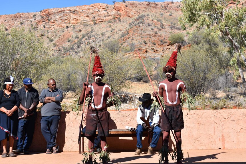 Two Aboriginal men traditionally painted, dancing in front of a range.