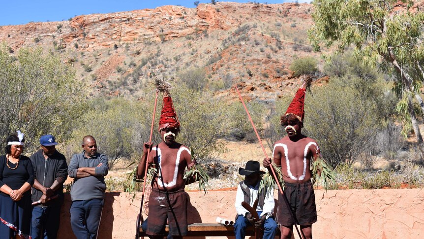 Two Aboriginal men traditionally painted, dancing in front of a range.