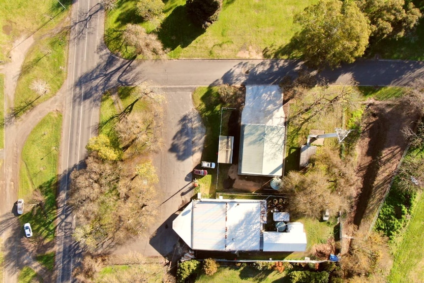 An aerial shot show a white-roof building surrounded by grass area and an unsealed road out the front.